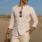 Man wearing a light-colored Ledbury button down shirt with rolled-up sleeves in a beach setting
