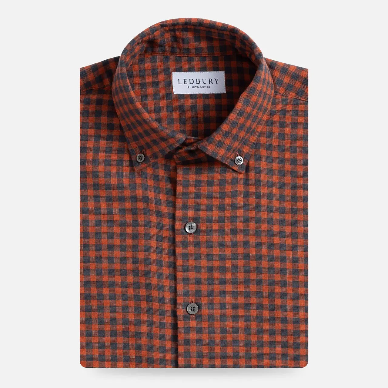 A folded men's button-down shirt by Ledbury, featuring a burnt orange and dark grey gingham check pattern, displayed on a clean light gray background.