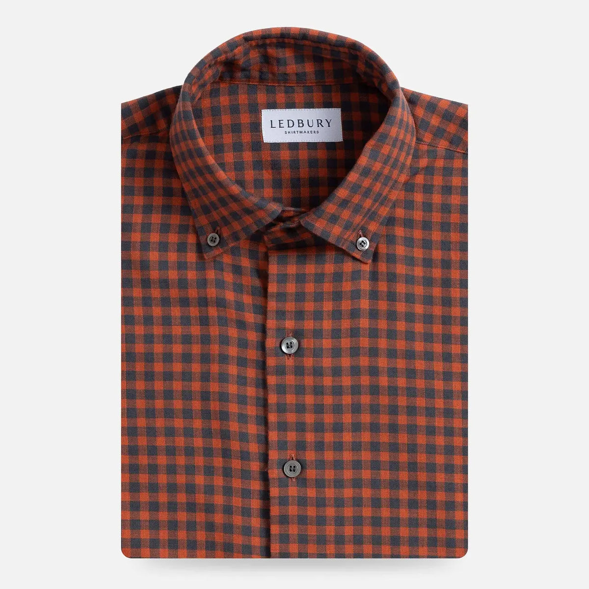A folded men's button-down shirt by Ledbury, featuring a burnt orange and dark grey gingham check pattern, displayed on a clean light gray background.