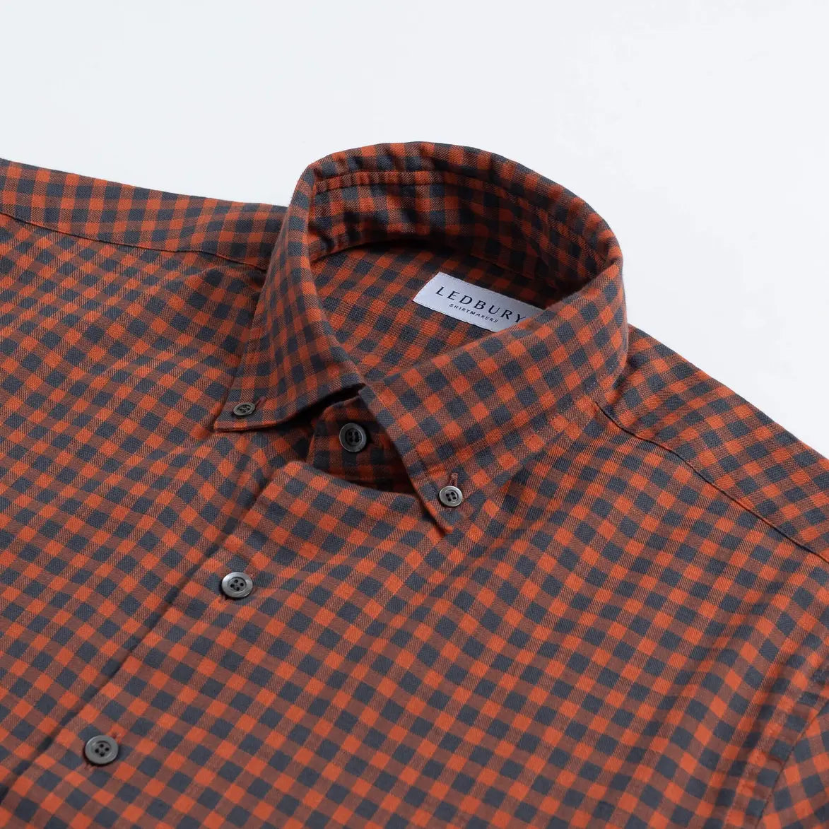 Close-up of a checkered button-down shirt collar in orange and dark gray, with a visible LEDBURY neck label.