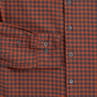 Close-up of a burnt orange and dark gray checkered plaid button-down shirt, showing a chest pocket with buttoned flaps and gray buttons.
