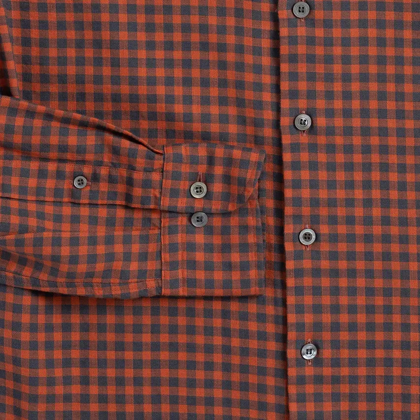 Close-up of a burnt orange and dark gray checkered plaid button-down shirt, showing a chest pocket with buttoned flaps and gray buttons.