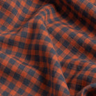 A close-up of draped fabric with a classic gingham pattern in rust orange and dark grey.