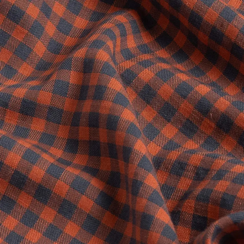 A close-up of draped fabric with a classic gingham pattern in rust orange and dark grey.