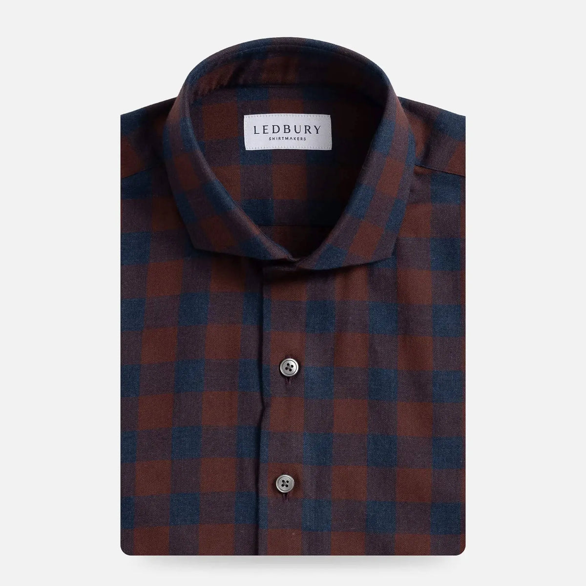 A folded men's dress shirt by Ledbury, featuring a classic checkered pattern in bordeaux red and navy blue. The shirt is neatly folded to show the collar, front button placket, and fabric texture against a clean, light gray background.