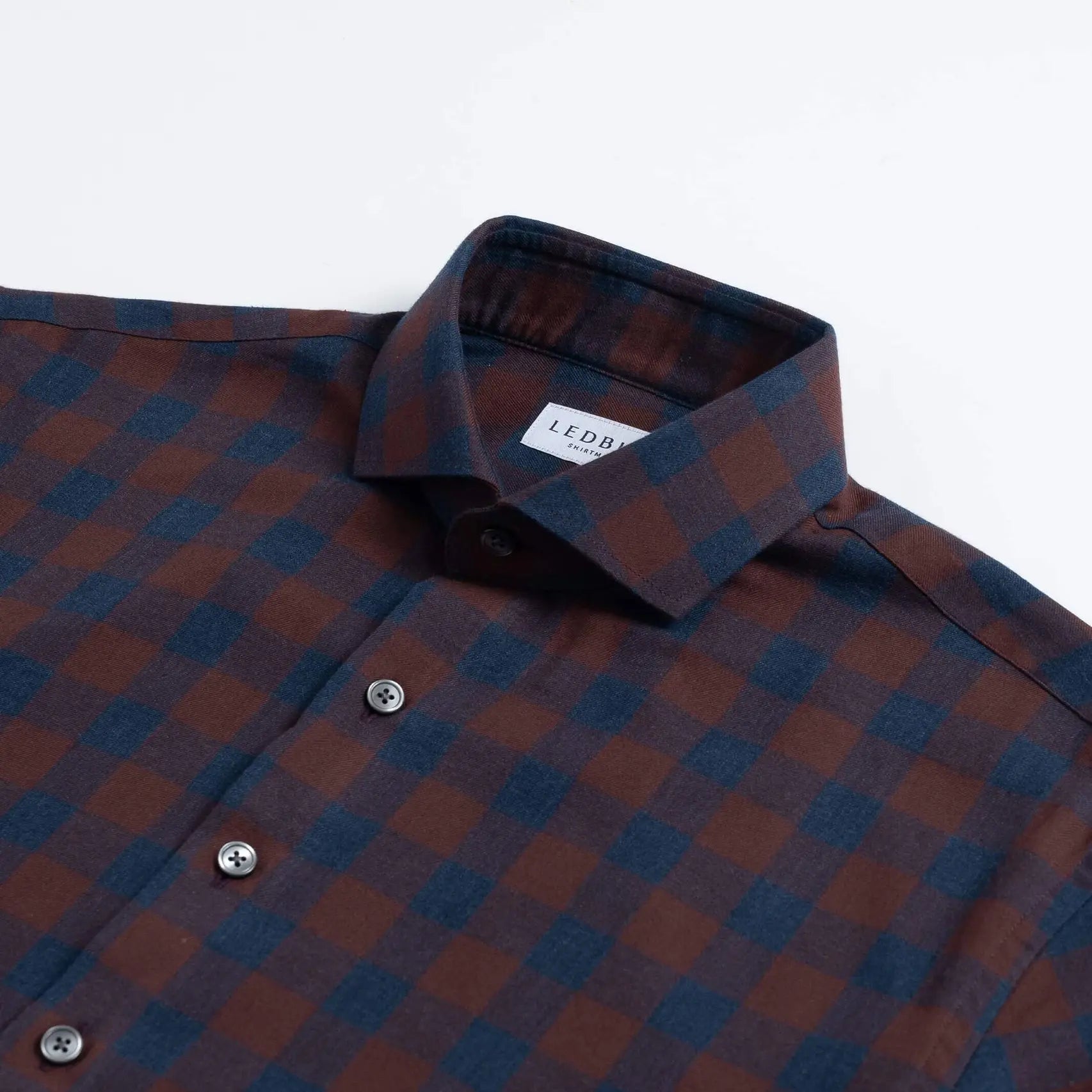 A close-up of a Ledbury brand long-sleeve button-down shirt featuring a dark red and navy blue checkered pattern, with a white neck label.