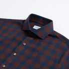 A close-up of a Ledbury brand long-sleeve button-down shirt featuring a dark red and navy blue checkered pattern, with a white neck label.