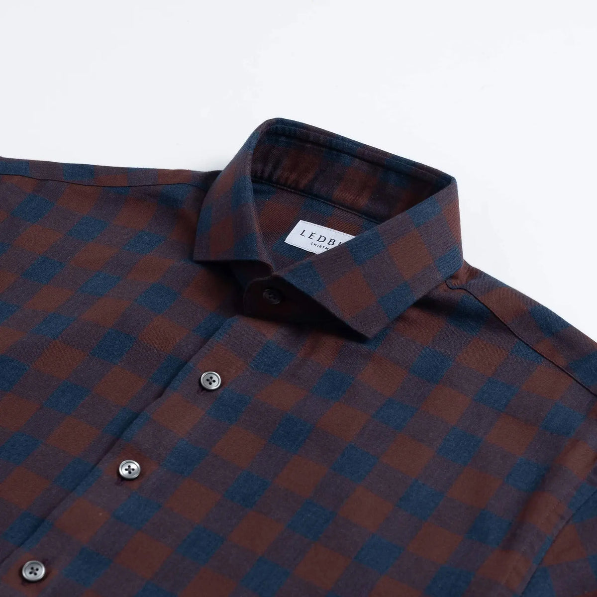 A close-up of a Ledbury brand long-sleeve button-down shirt featuring a dark red and navy blue checkered pattern, with a white neck label.
