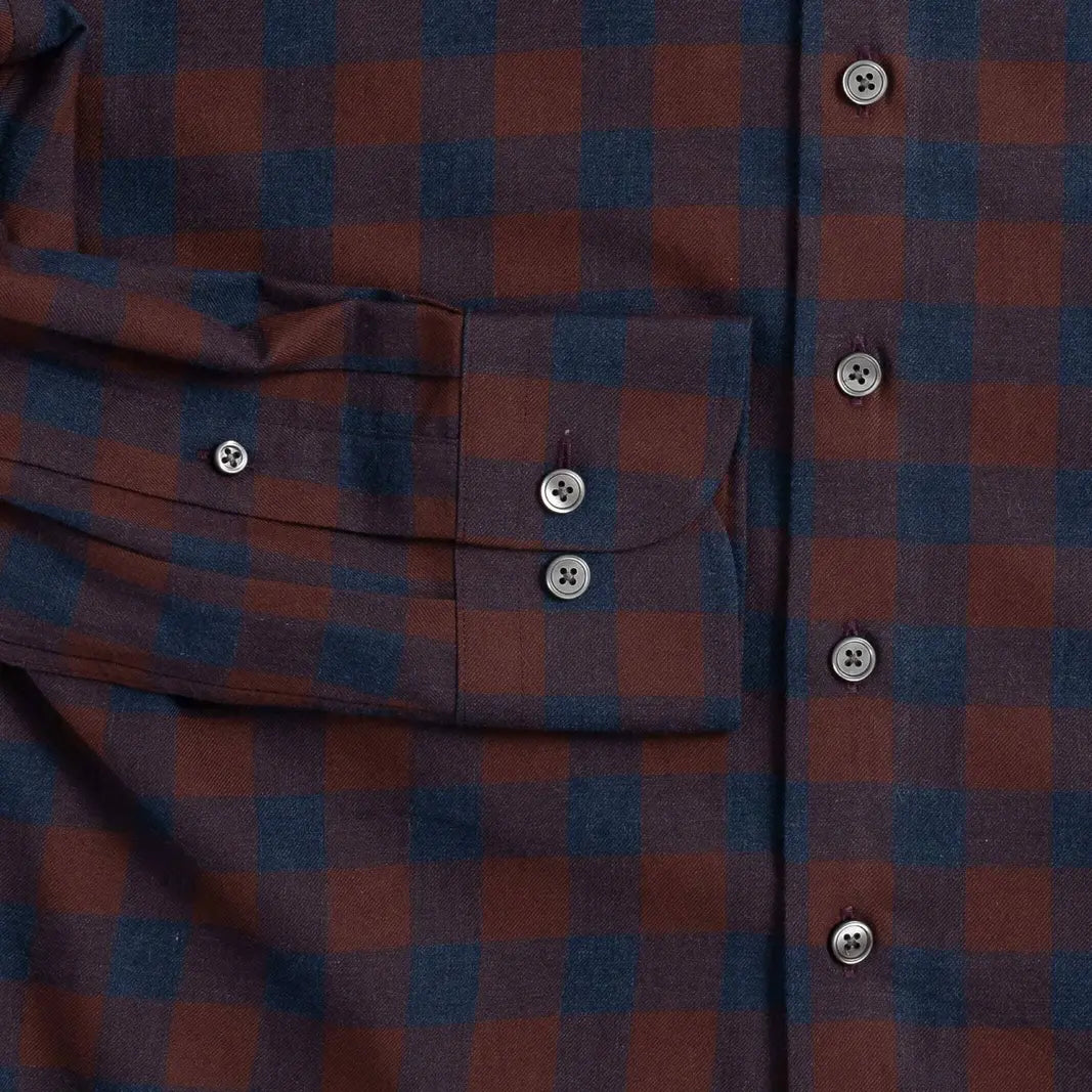 Close-up of a plaid button-up shirt in dark red and navy blue, showing a chest pocket with a flap and smoke grey buttons.